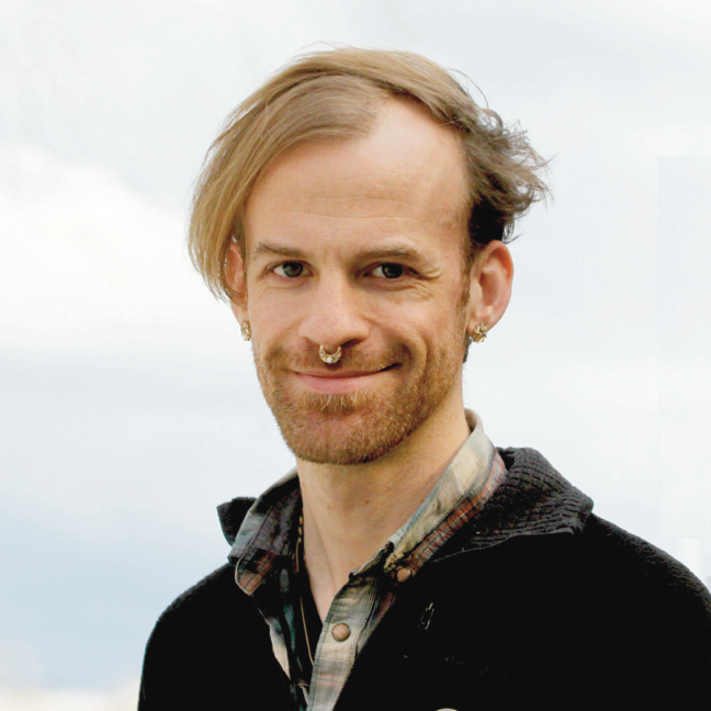 Portrait of Sasha Strong. Sasha is a white person wearing a gold nose ring, a plaid shirt, and a black jacket. The background is a grey sky.