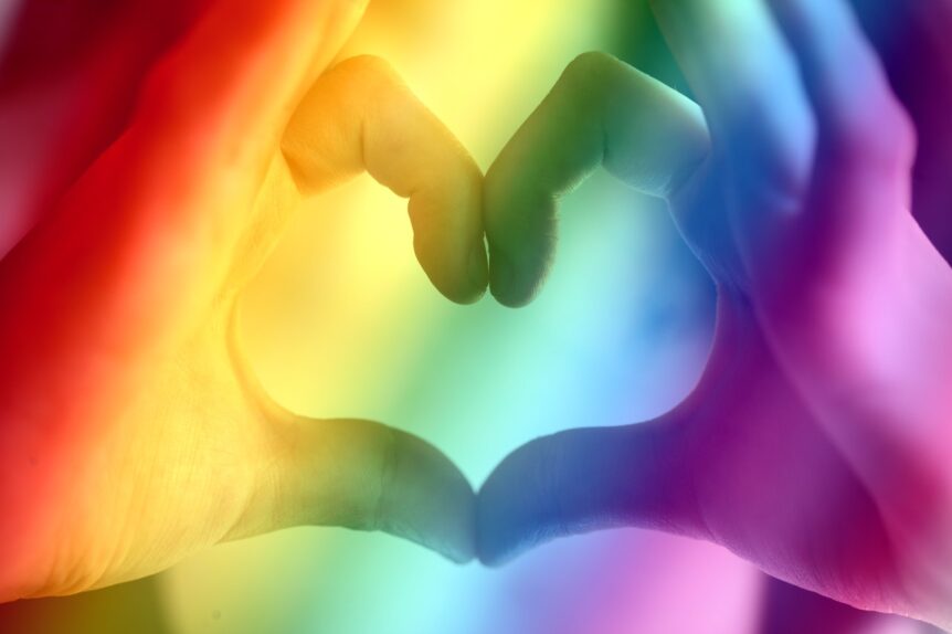 Two hands with thumbs and forefingers forming a heart shape, with a raindow stripe filter over all.