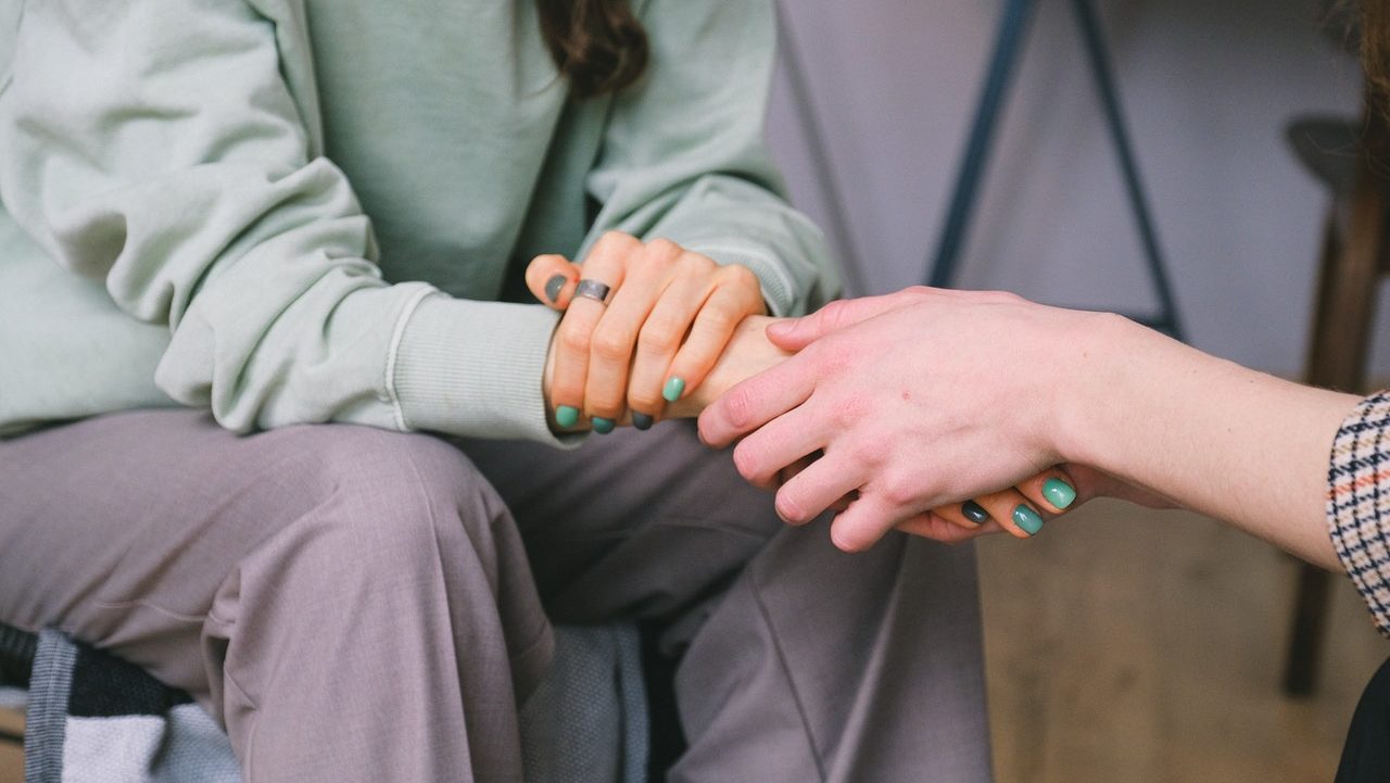 Close up of hands of two people sitting across from each other in a room. The image suggests gentle support.